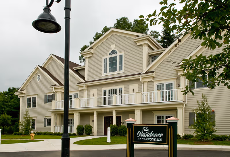 A large beige senior living facility with balconies and a front entrance sign.