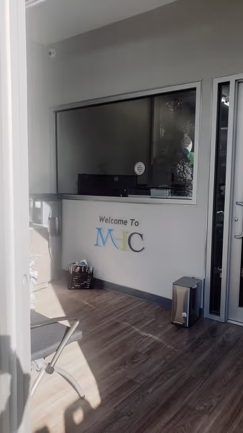 Reception area with a glass window, Welcome To MHC sign, and wood floor.
