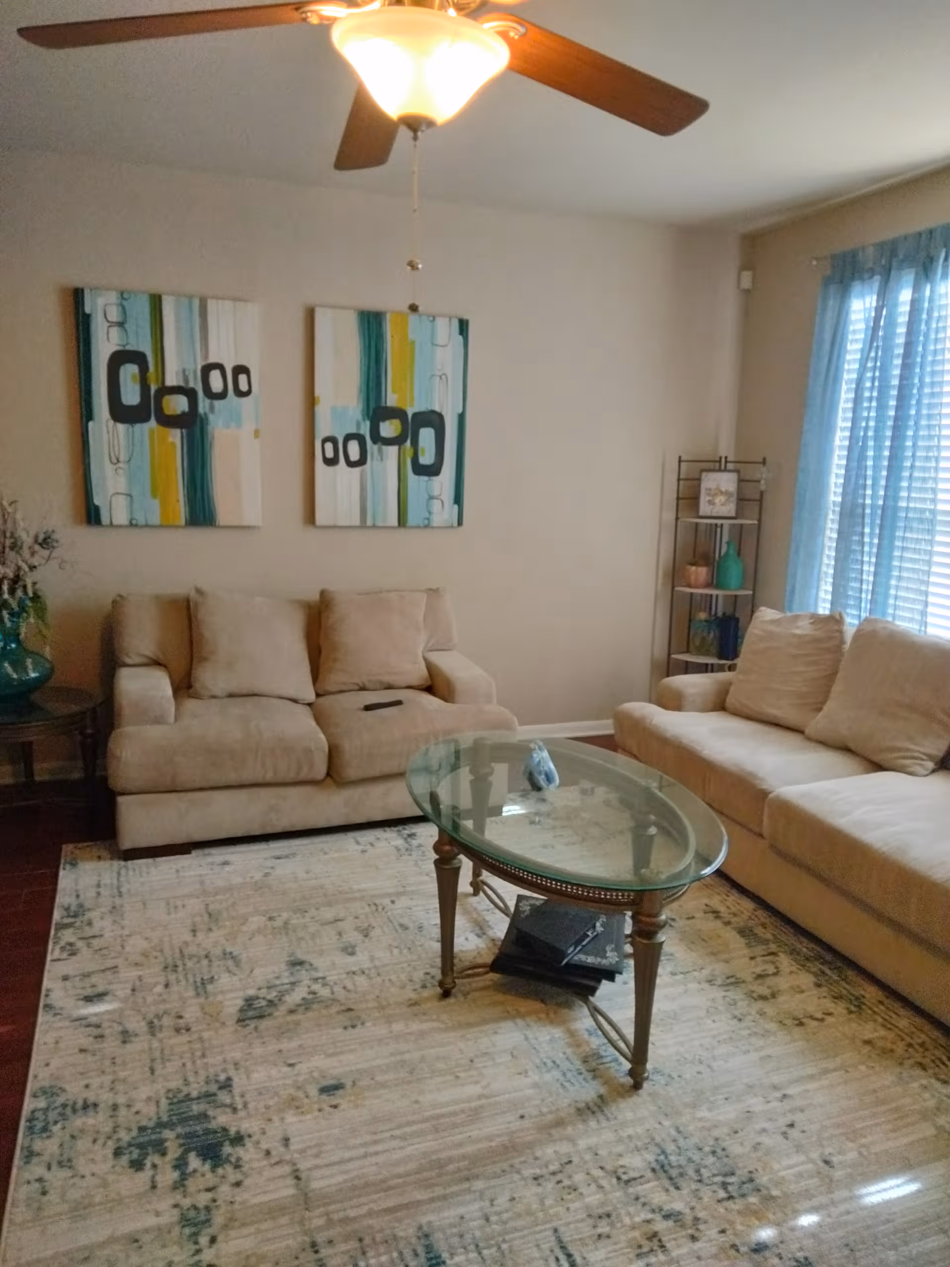 Comfortable beige living room with sofas, glass coffee table, rug, and abstract teal art.