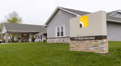 Exterior view of Homestead Assisted Living of Derby building with a well-maintained green lawn in front and a sign displaying the facility's name and address, 701 Mount Grove Road.