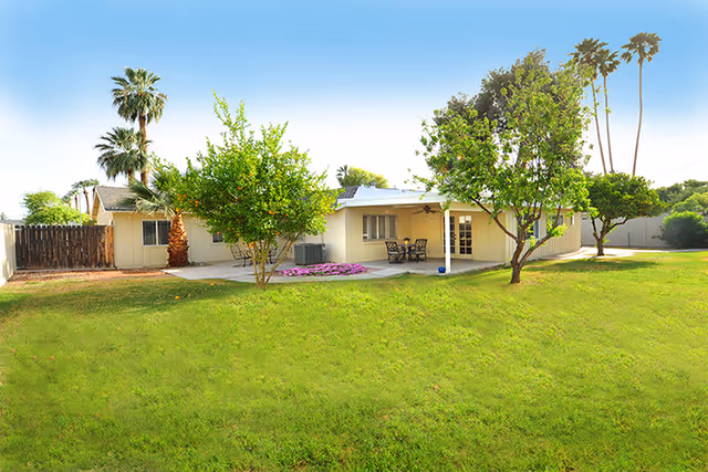 Front view of a single-story assisted living facility with a grassy lawn and shaded patio.