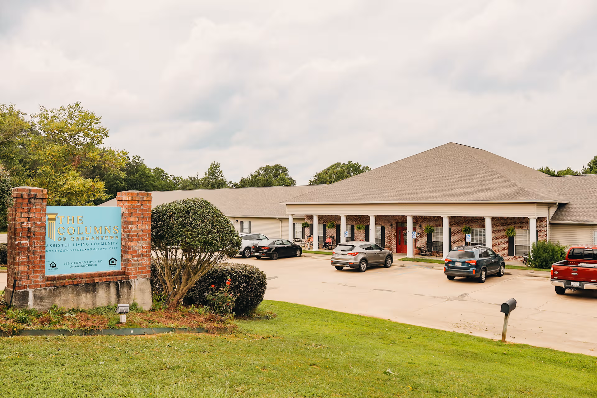 Exterior view of The Columns of Germantown with brick entrance, columns, and cars parked in front.