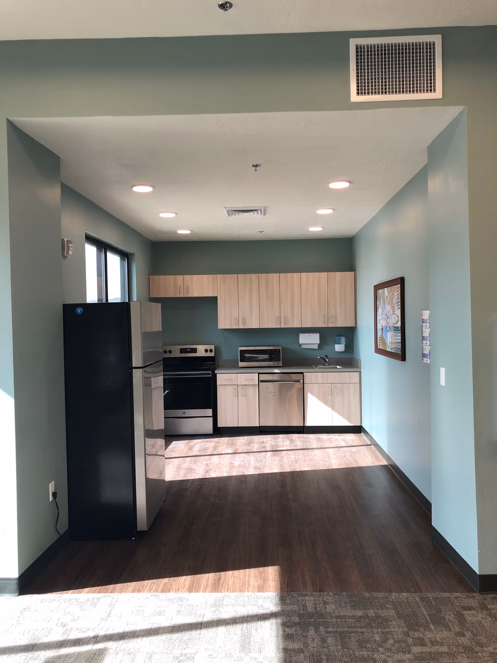 Small modern kitchen with fridge, stove, dishwasher, and light wood cabinets.