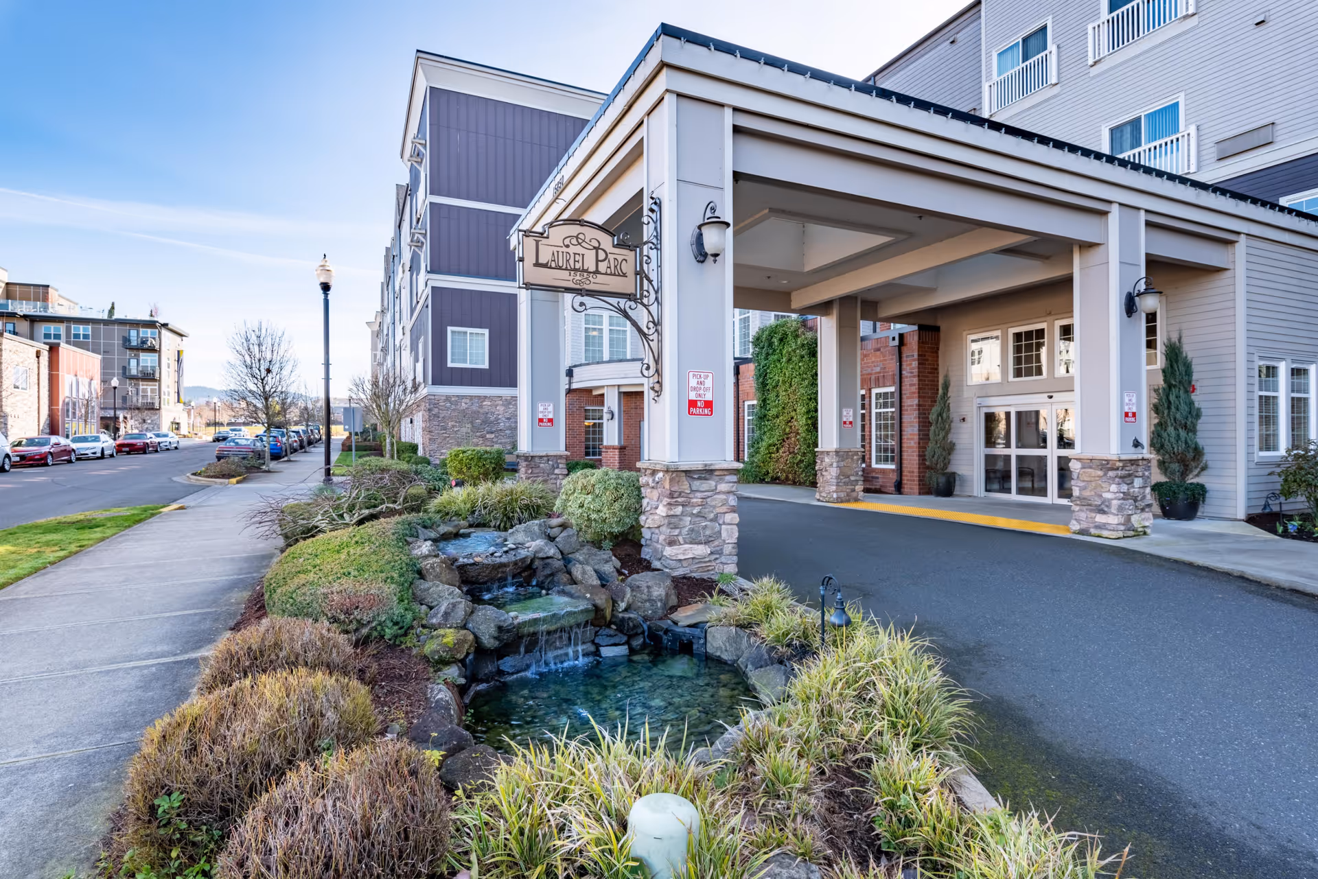 Exterior view of Laurel Parc Senior Living entrance with a covered driveway and landscaped water feature.