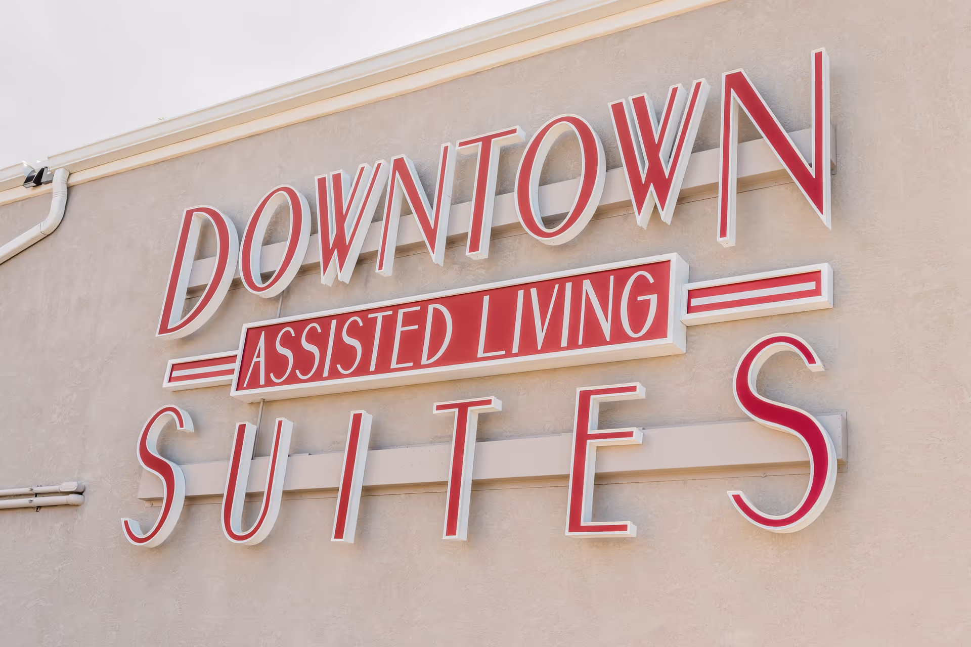 Exterior wall sign of Downtown Assisted Living Suites with large red and white letters mounted on a beige stucco wall.