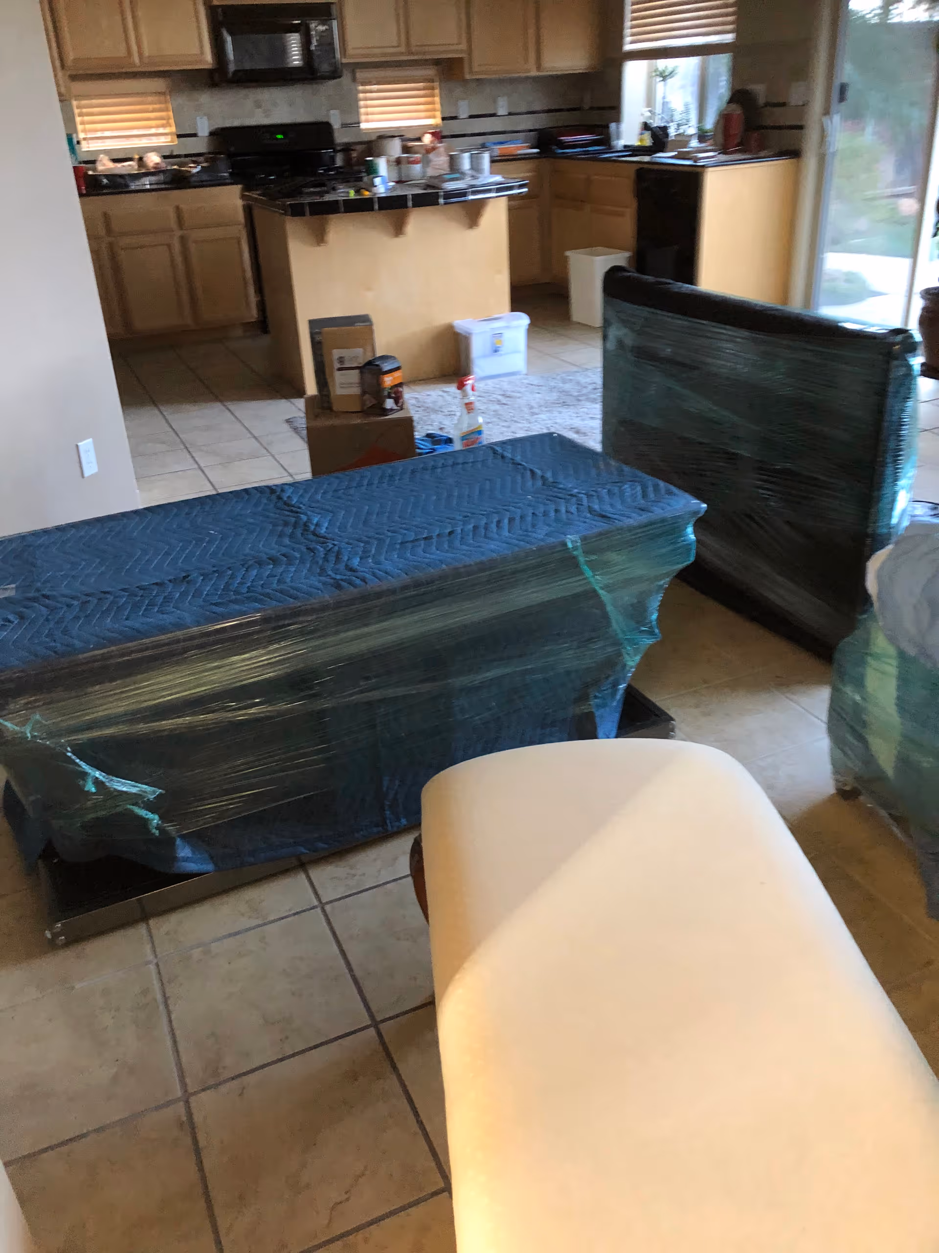 Interior kitchen and living area with wrapped furniture and moving boxes in a senior living facility.