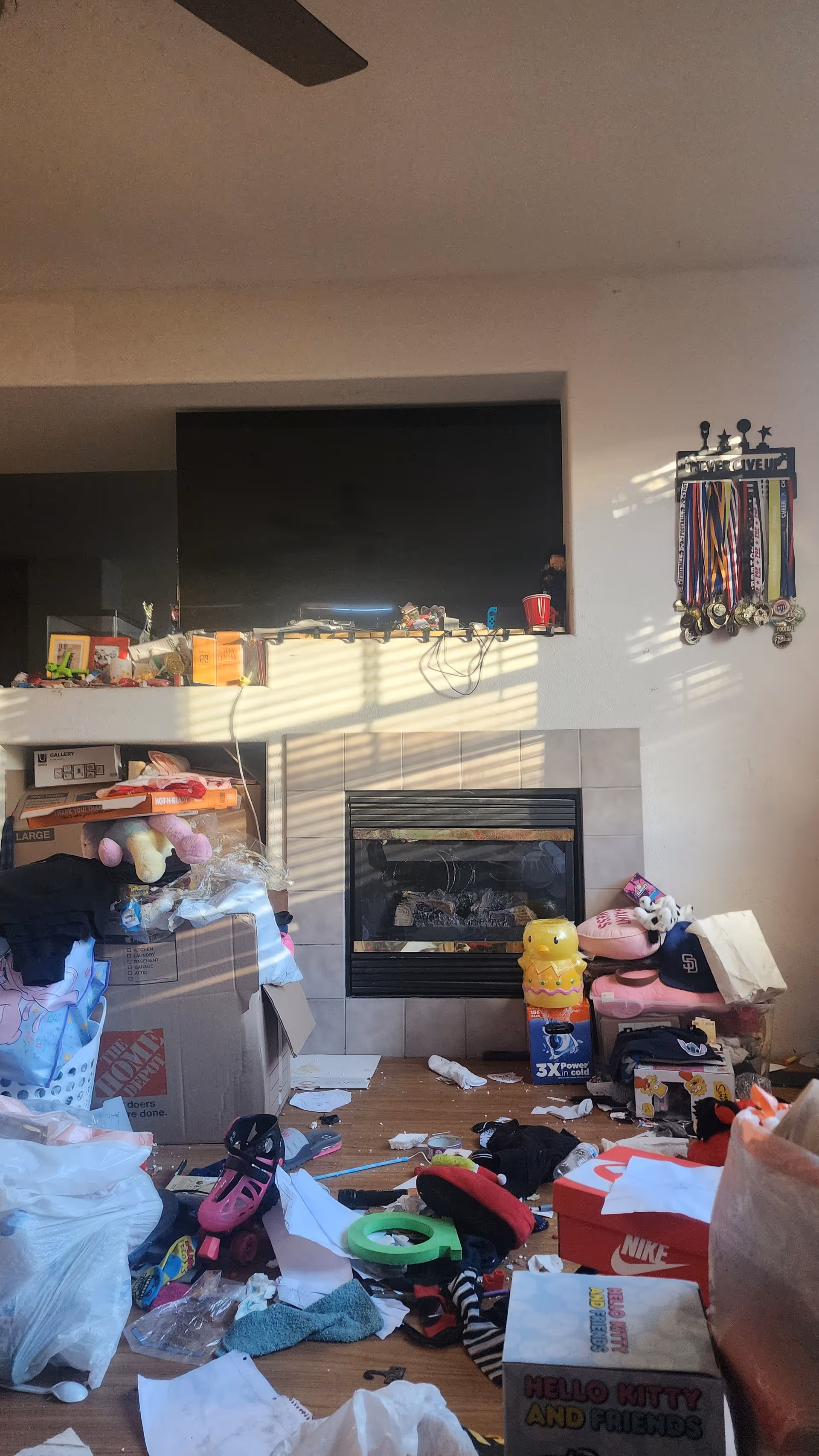 A cluttered living room with a TV above a fireplace and scattered toys and boxes.