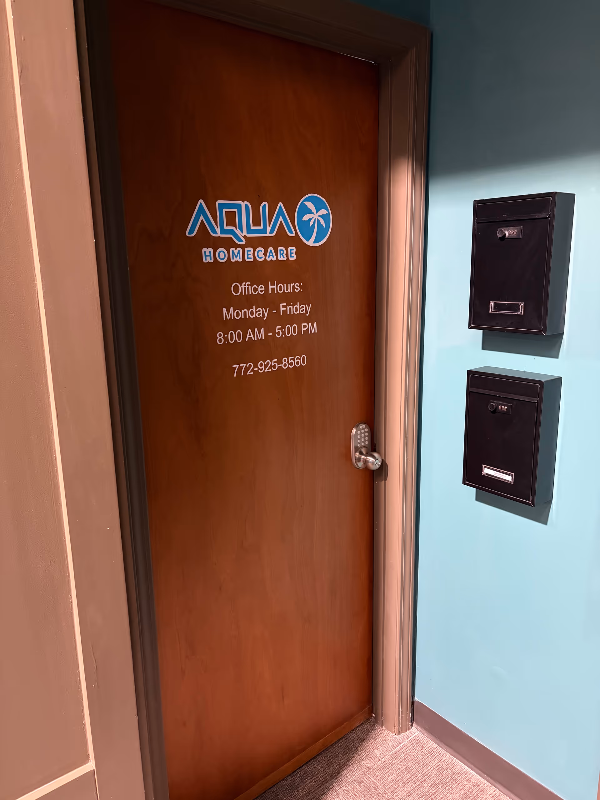 Wooden door labeled Aqua Home Care with hours, flanked by mailboxes on a teal wall.