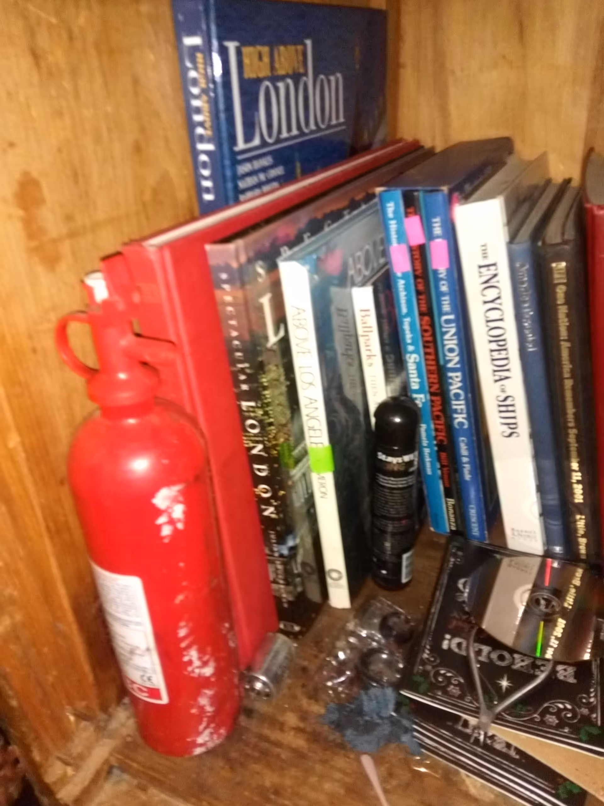 Wooden shelf with red fire extinguisher and assorted books in a cluttered corner.
