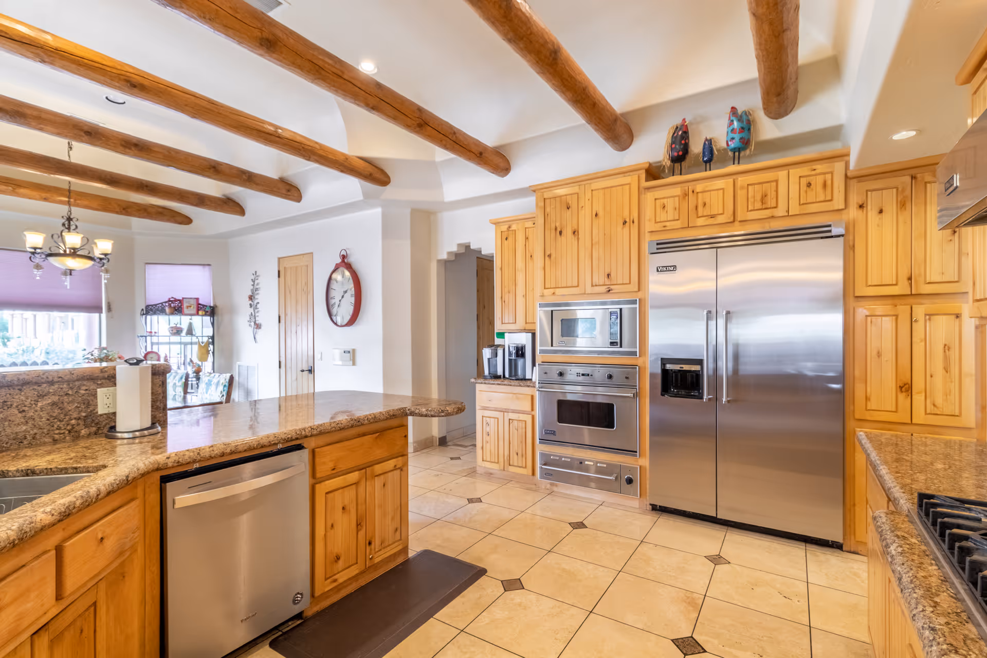 Bright kitchen with granite countertops, wooden cabinets, stainless appliances, and exposed beams.