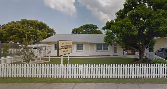 Front view of a single-story assisted living facility with a white picket fence and sign.