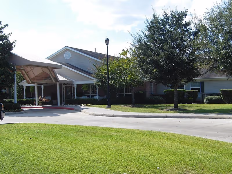 Senior living facility entrance with covered drop-off, lawn, and trees.
