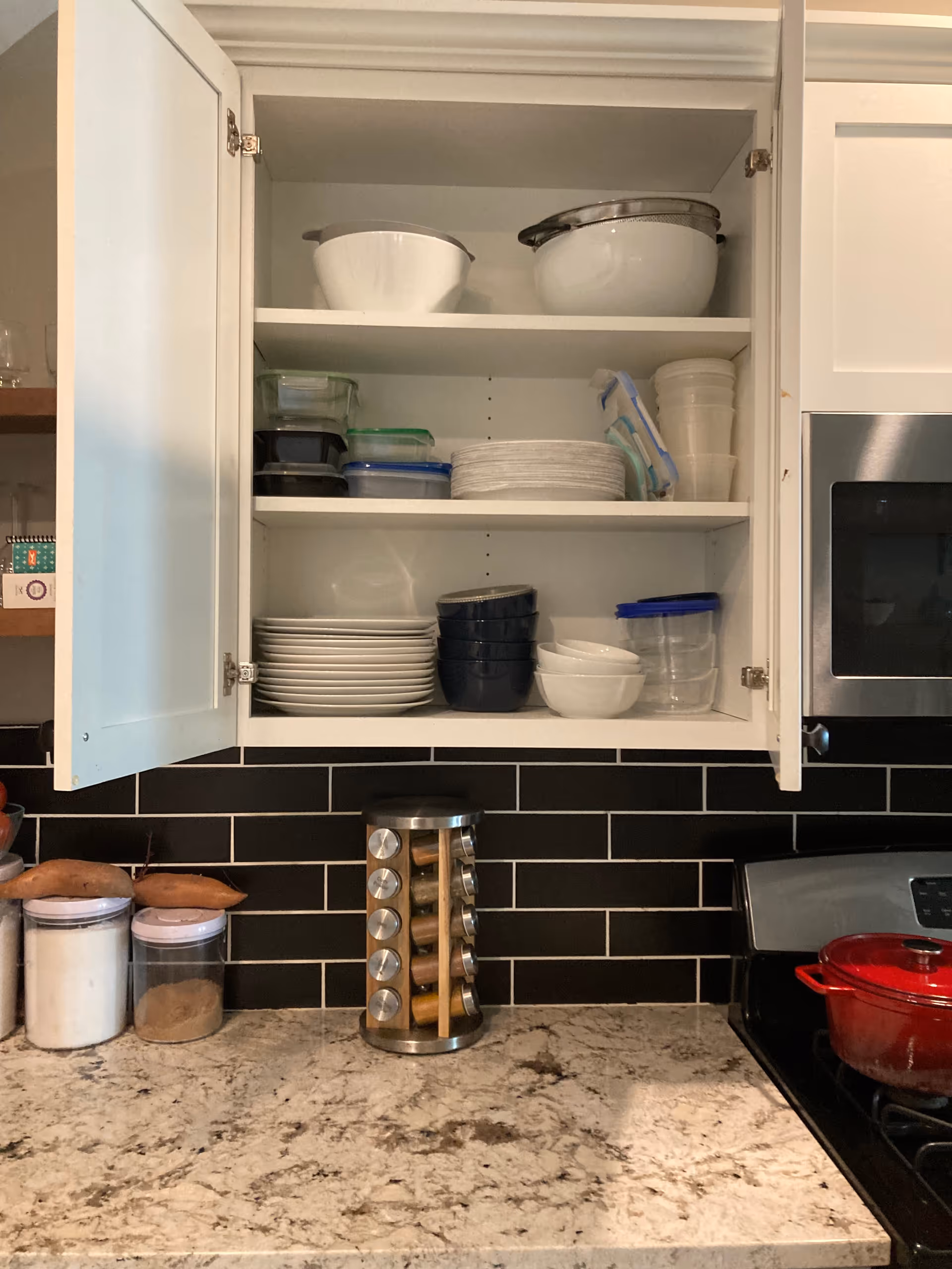 Open kitchen cabinet displaying dishes, bowls, and a spice rack on the countertop.