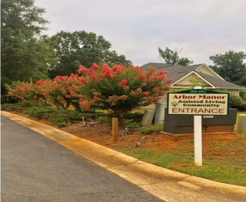 Exterior view of Arbor Manor entrance with flowering shrubs and sign.