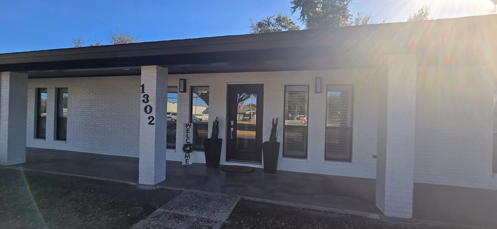 White brick senior facility exterior with pillar 1302, glass doors, windows, and sun glare.