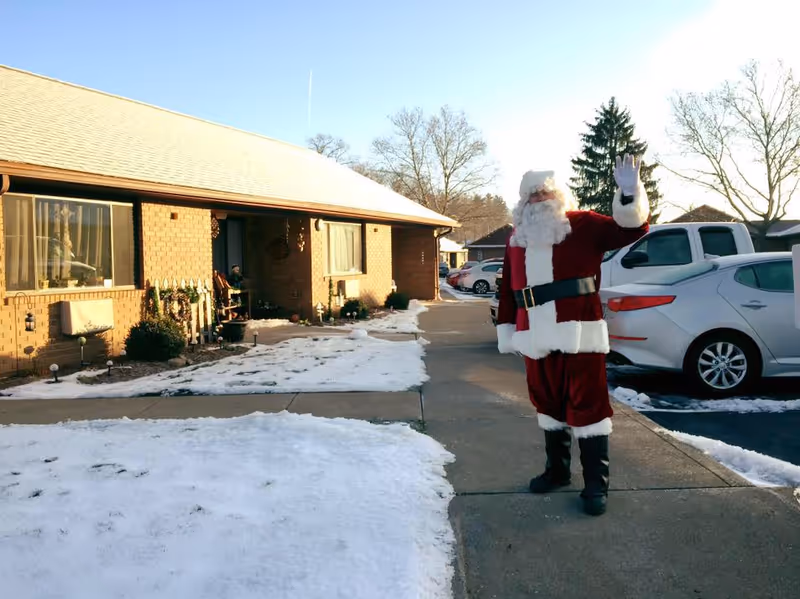 Santa waves outside Norton Guest Home on a snowy sidewalk.