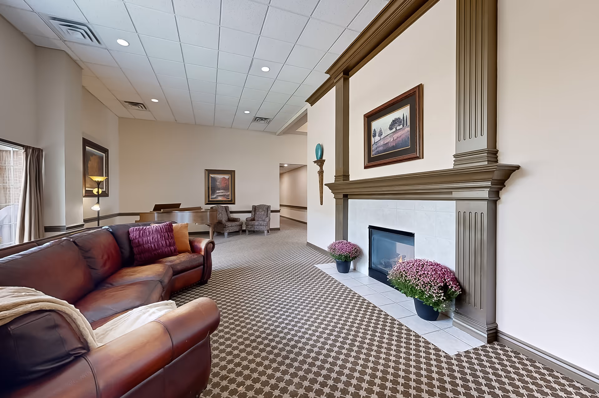 Spacious lobby seating area with leather sofa, fireplace, framed art, and potted flowers.