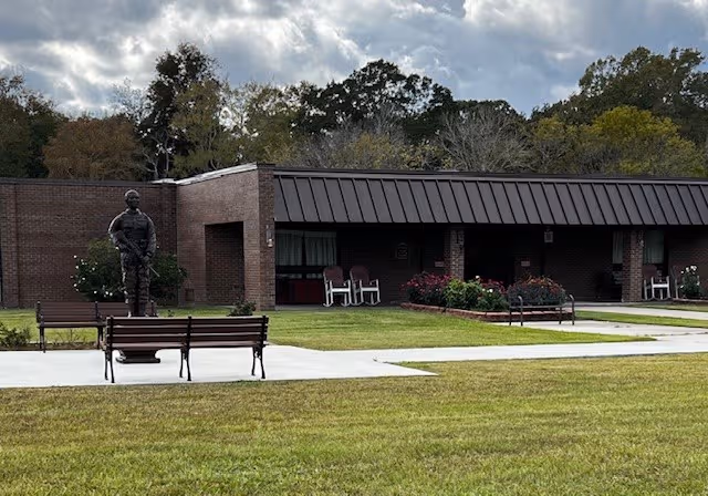 Brick exterior with a statue, benches, and a shaded front porch on a grassy lawn.
