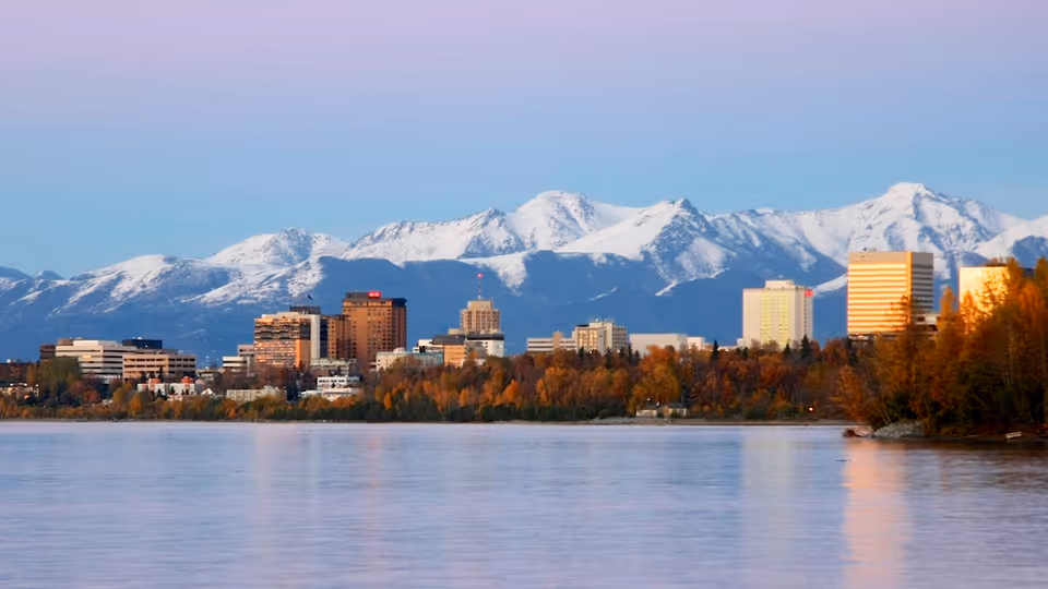 A waterfront city skyline with mountains in the background and calm water in foreground.