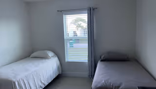 Two single beds sit in a small bedroom with a window between them and curtains.