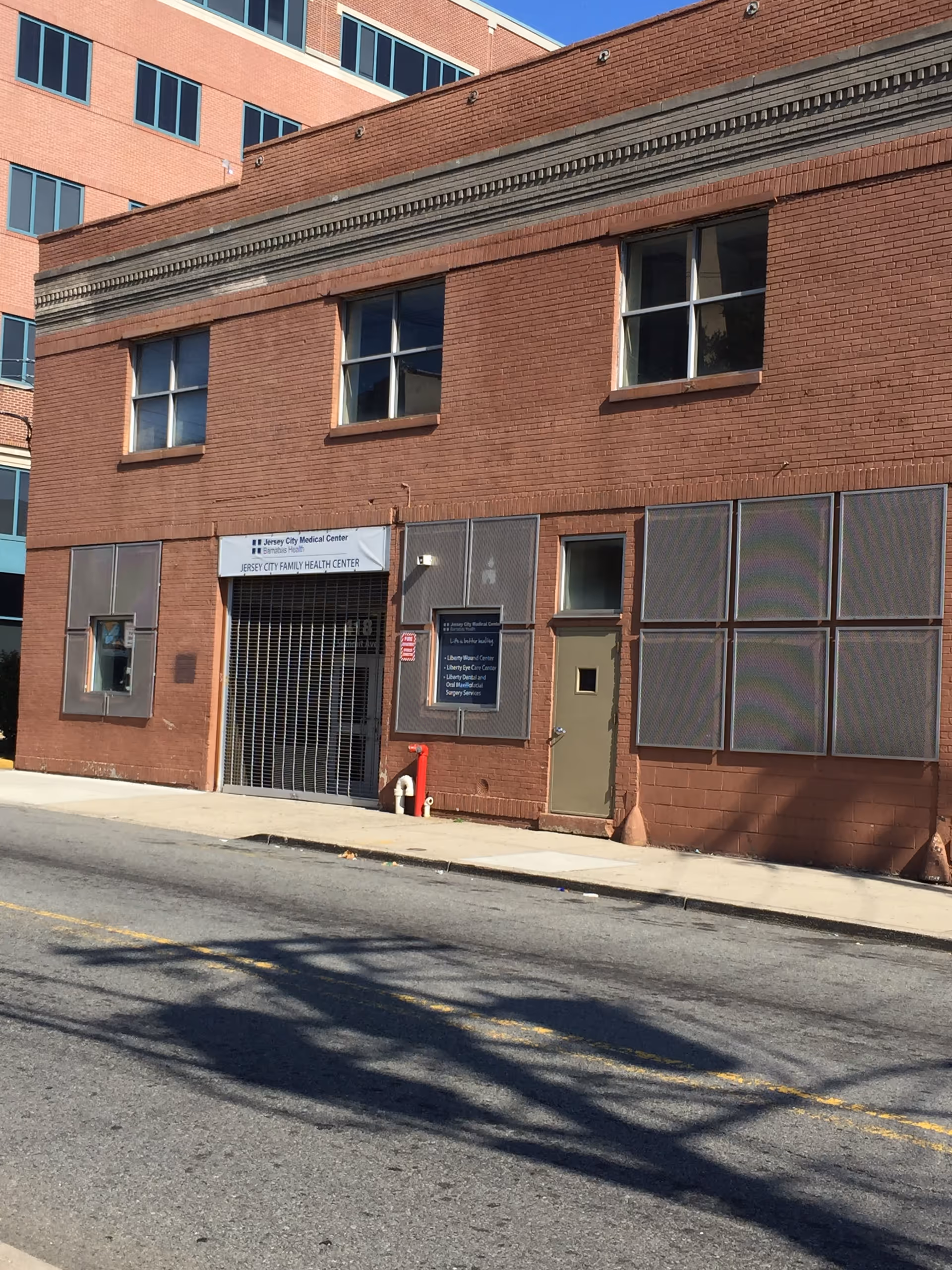 Red brick Liberty Healthcare building on a city street with signs and a gated entrance.
