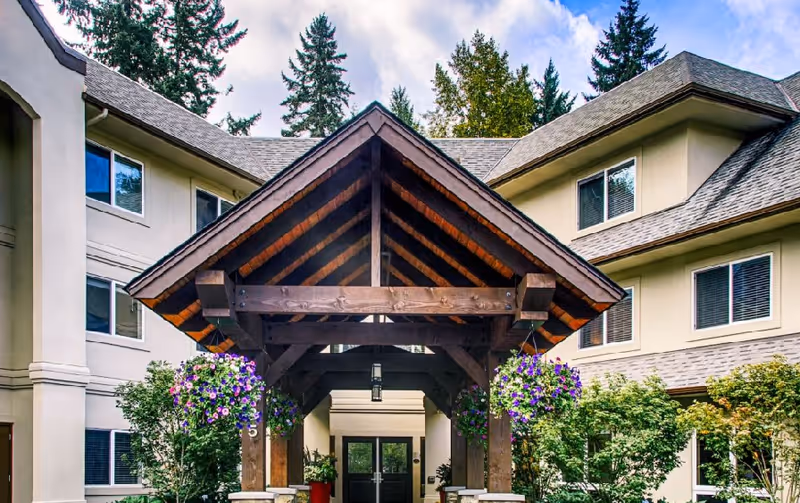Entrance of a senior living facility with a wooden peaked canopy and hanging flower baskets.