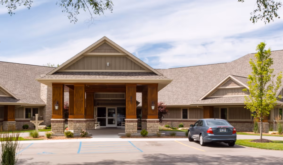 Front entrance of a tan senior living facility with a car parked nearby