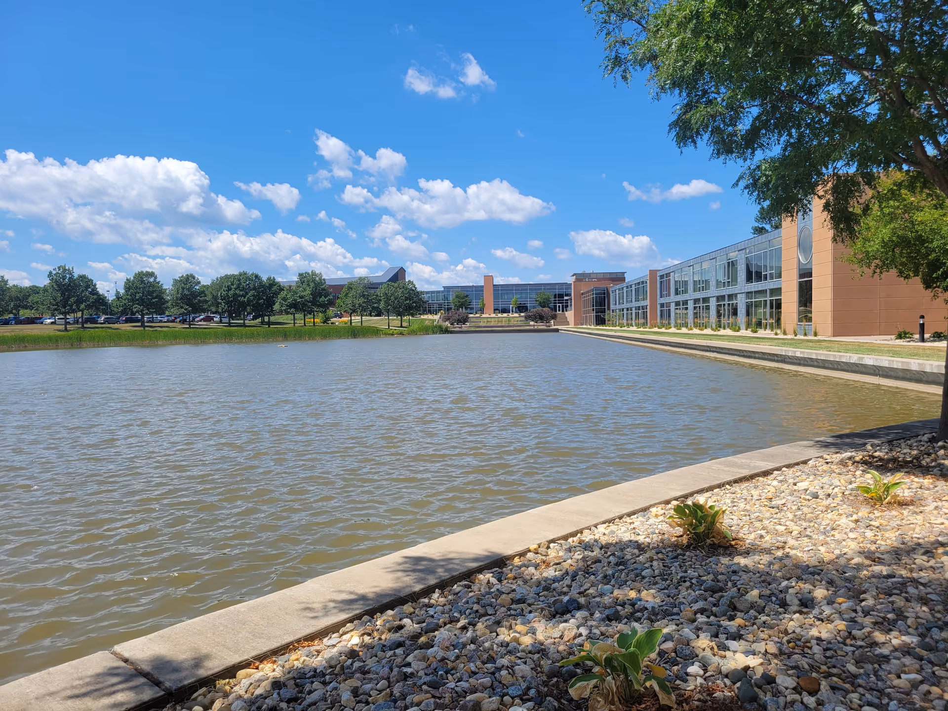Wide view of a modern senior living campus exterior with a pond and clear blue sky.