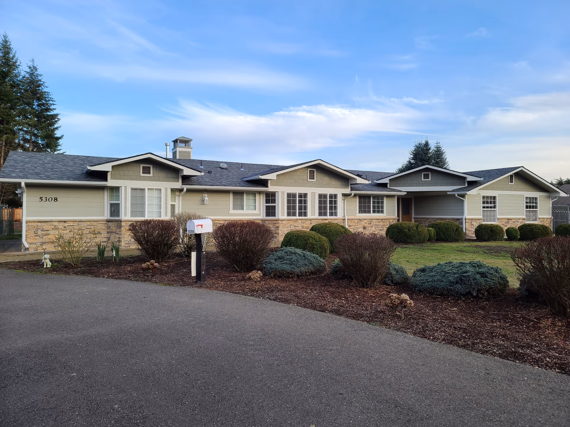 Single-story senior living facility with beige siding, stone accents, and a landscaped front yard.