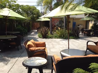 Courtyard patio with wicker chairs, round tables and green umbrellas surrounded by tropical plants.