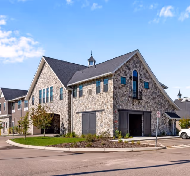 Stone-faced senior living building with a large front entrance under a blue sky.