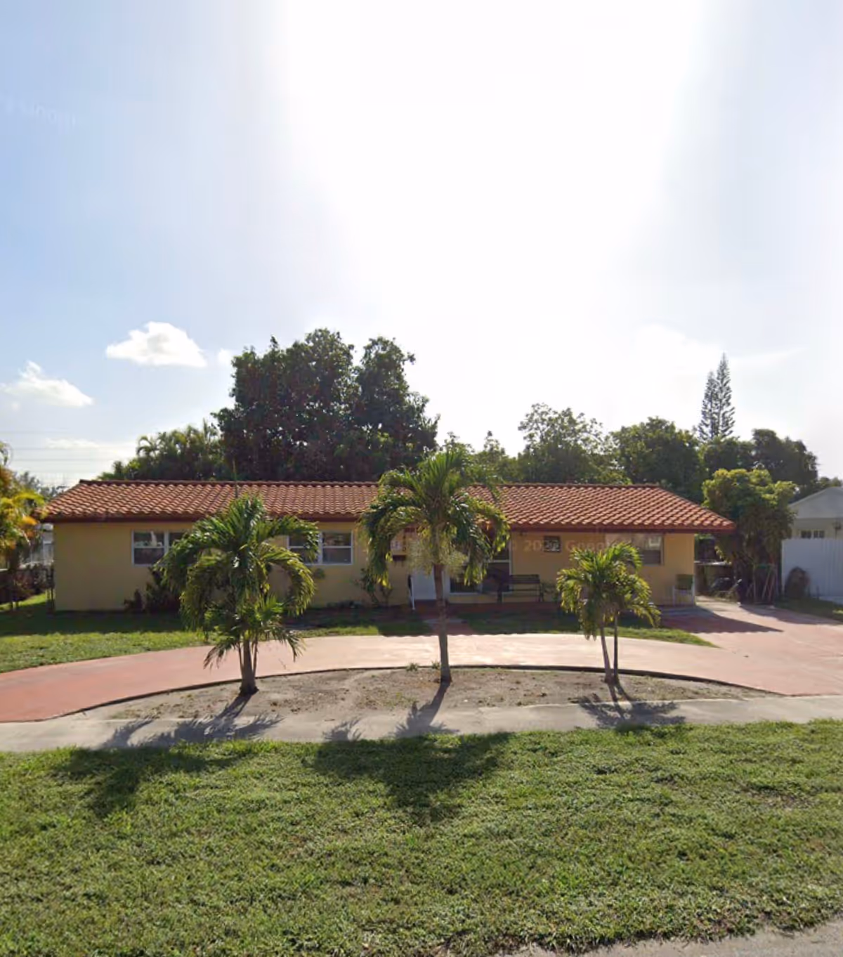 Single-story yellow building with red-tiled roof, palm trees, and a curved front driveway.