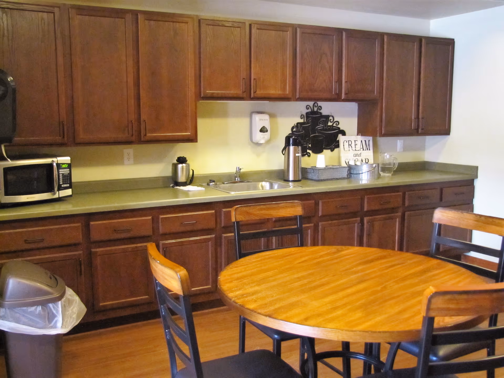 A kitchen with dark wooden cabinets, countertop appliances, and a round dining table with chairs.