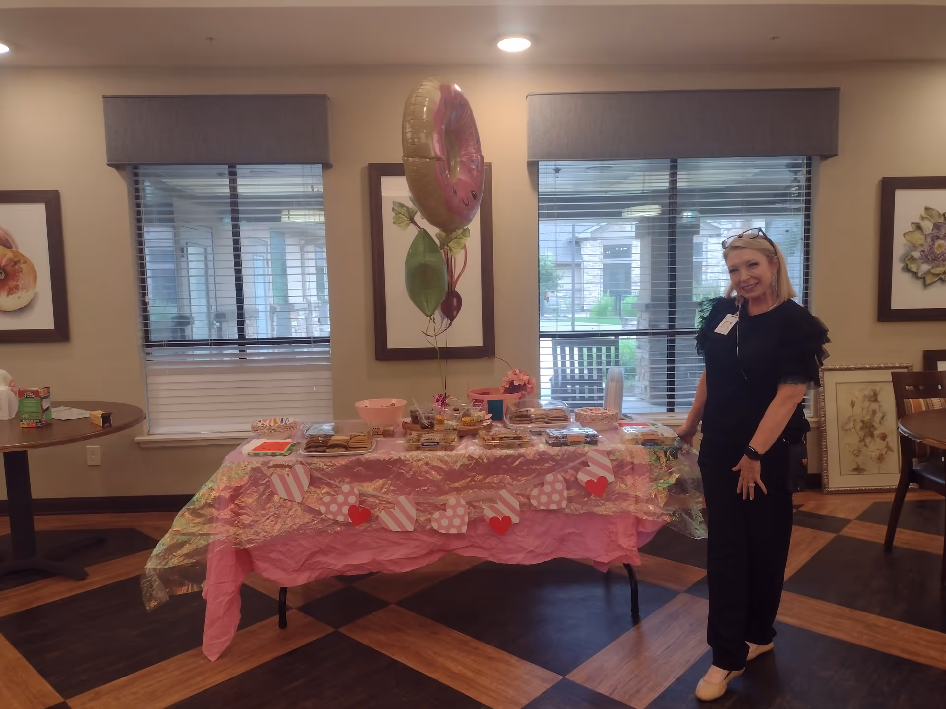 A staff member stands beside a decorated table with snacks in a senior living common area.