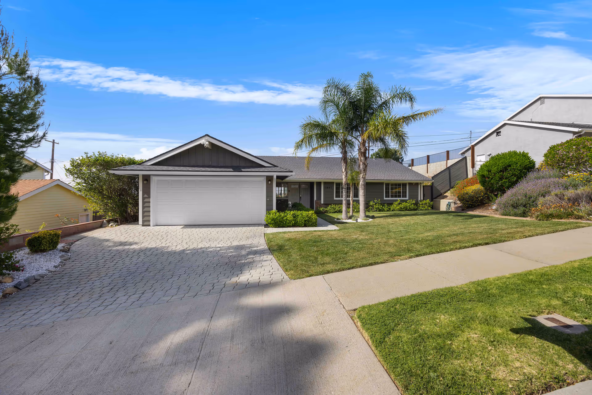 Exterior view of a single-story home with a two-car garage, palm trees, and a manicured lawn.