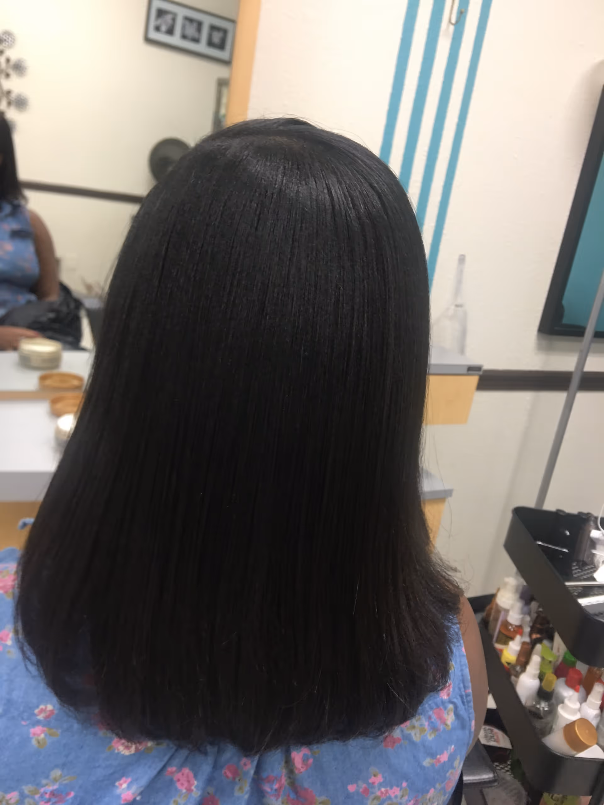 Back of a person with straight black hair at a salon workstation.
