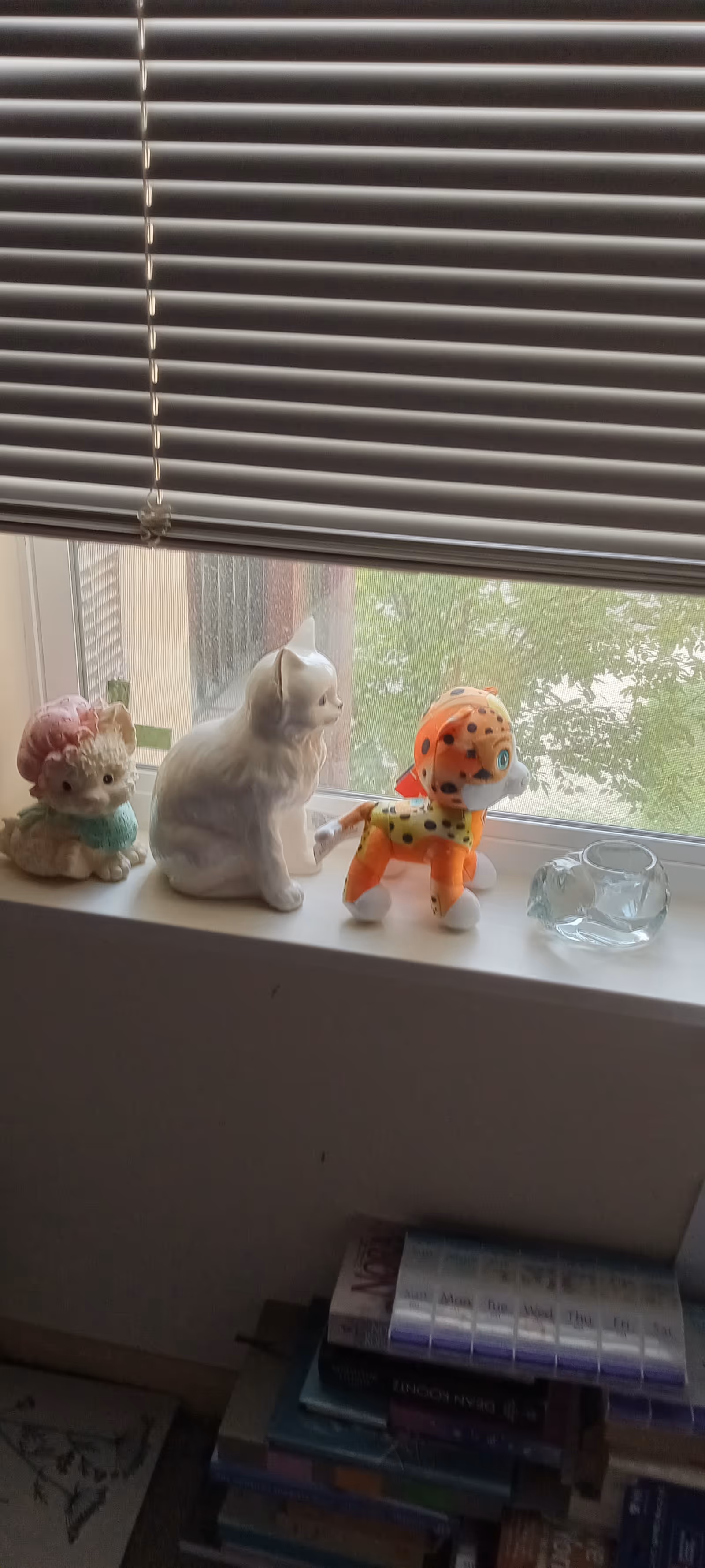 Window blinds above a windowsill with stuffed animals and a glass bowl.