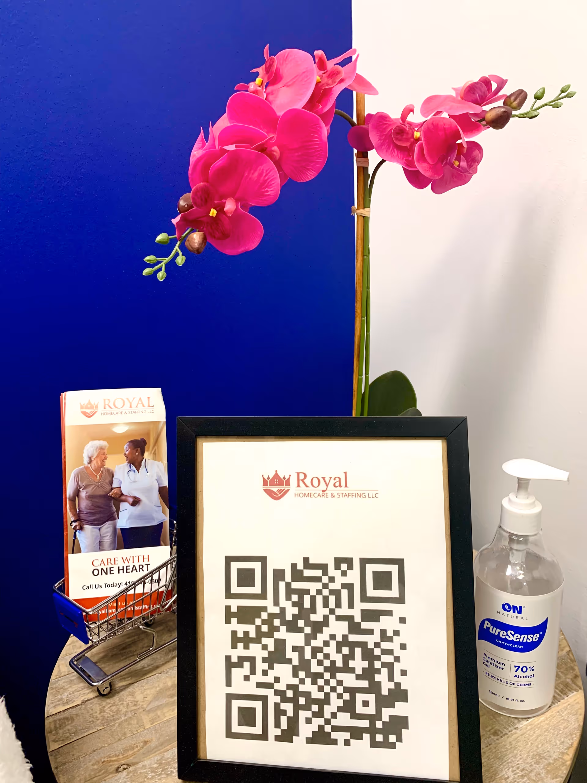 Interior desk area with pink orchid, QR frame, brochure rack, and hand sanitizer.