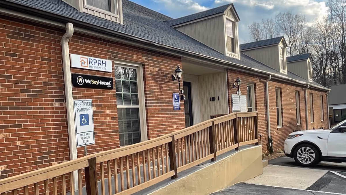 Brick building with a wooden ramp, handicap parking sign, and a white car at the entrance.