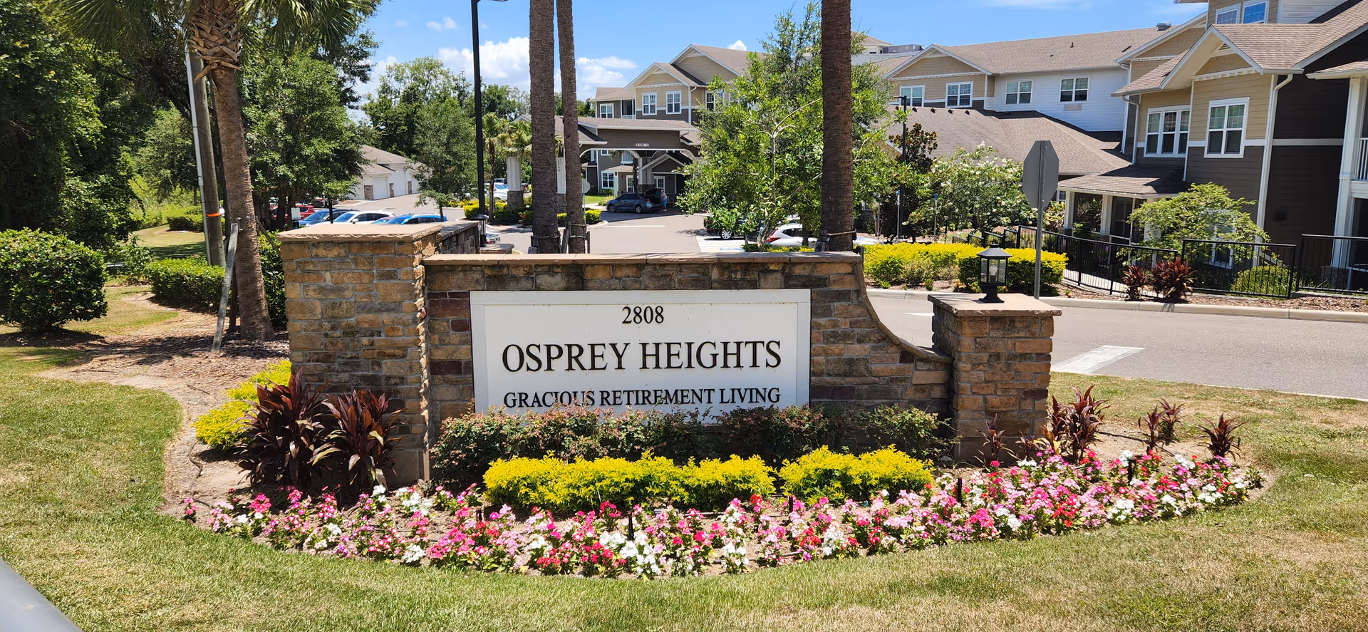 Exterior view of Osprey Heights sign with landscaped entrance and townhomes in background.