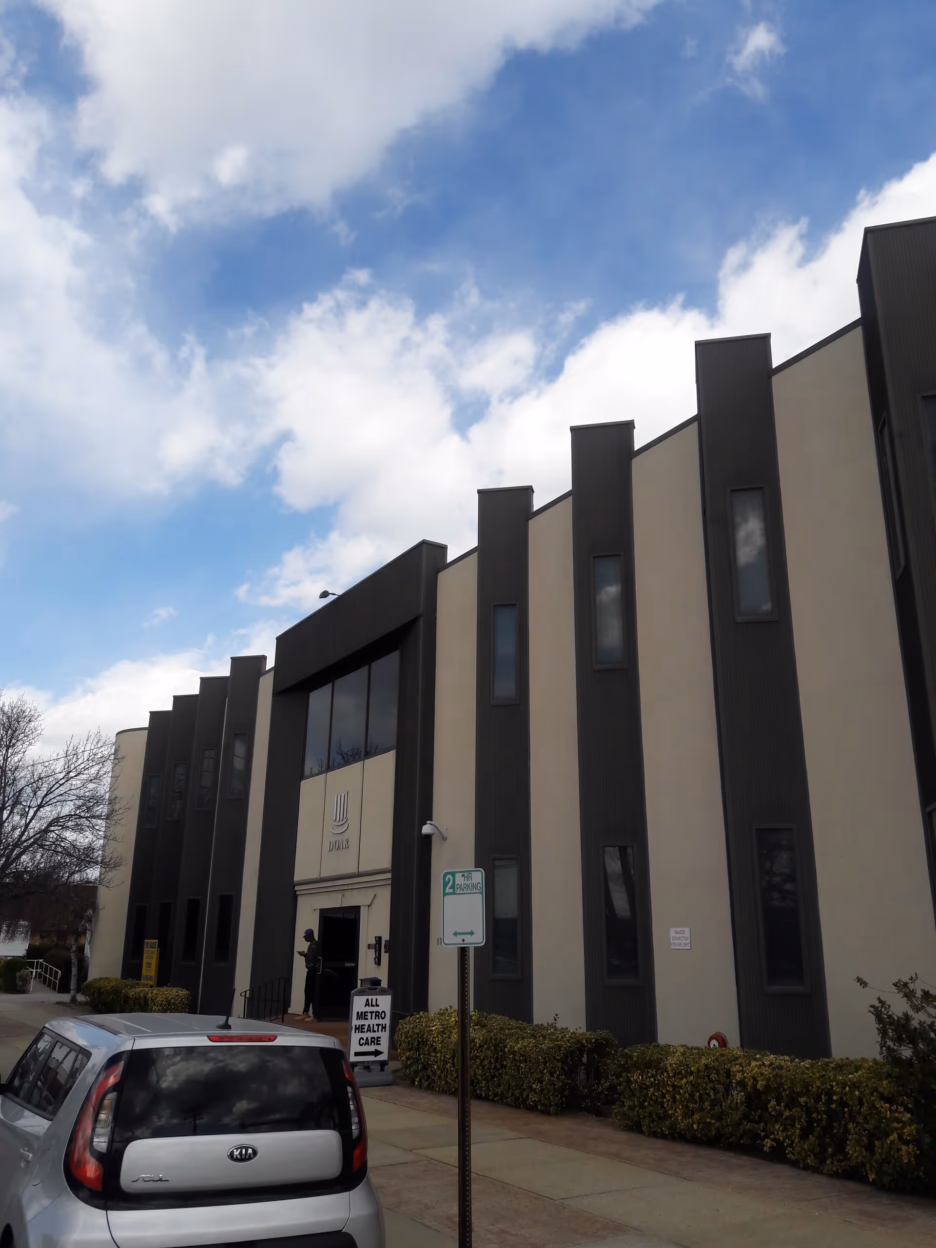 Exterior view of All Metro Health Care building with dark vertical panels and entrance sign.