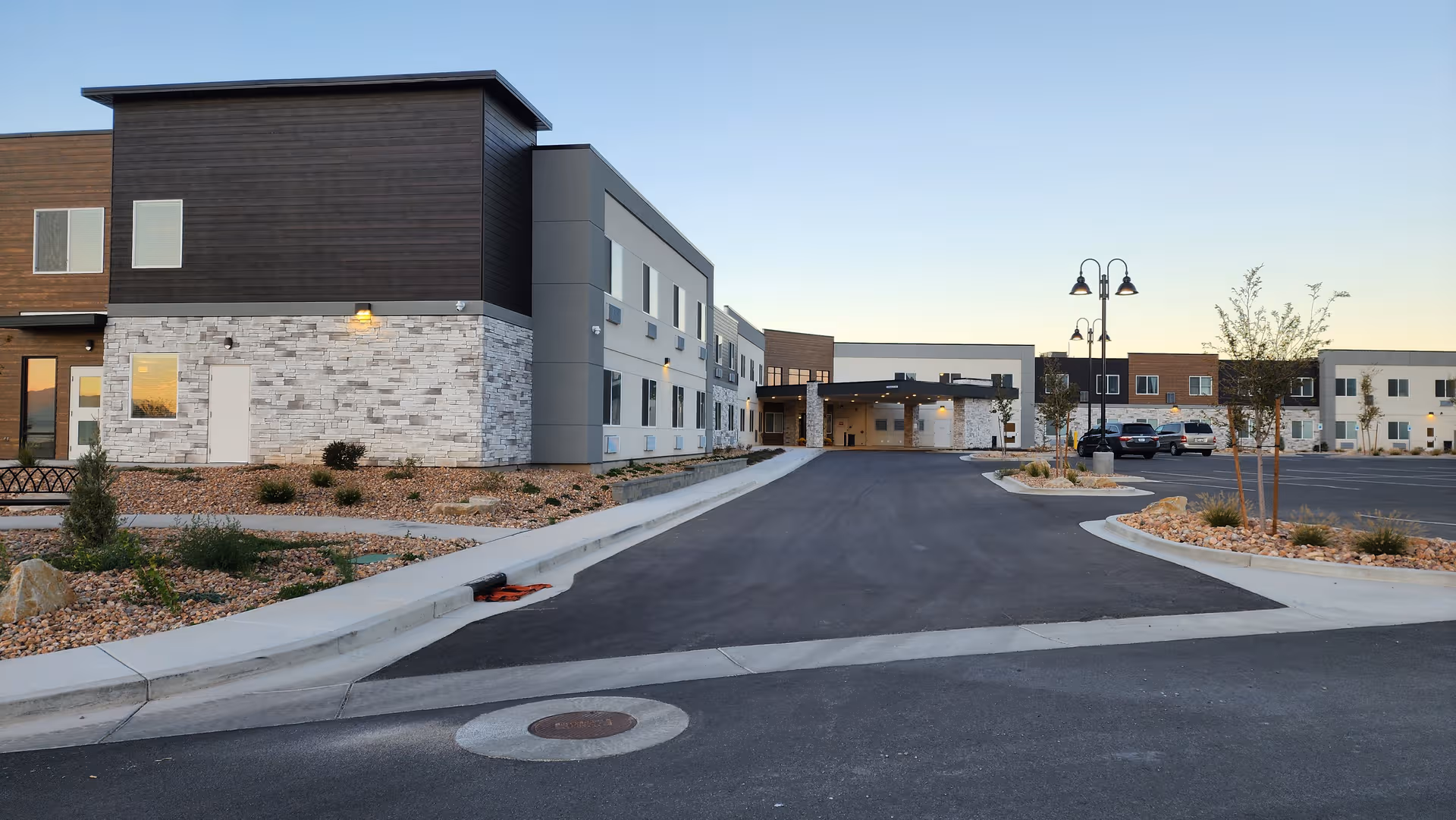 Modern senior living facility exterior with driveway, entrance, and landscaped surroundings.