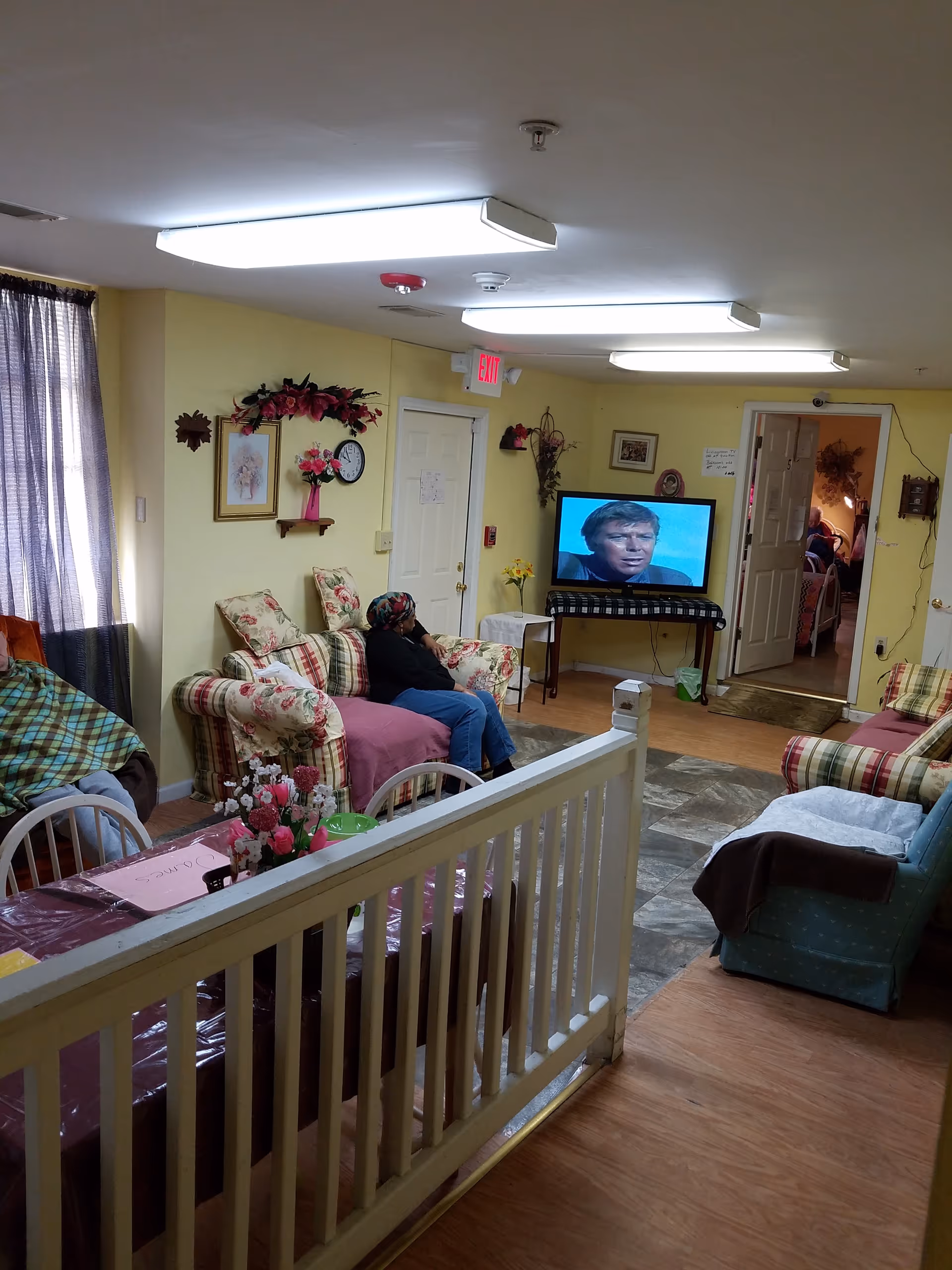 Residents relax in a cozy living room with floral couches and a TV.