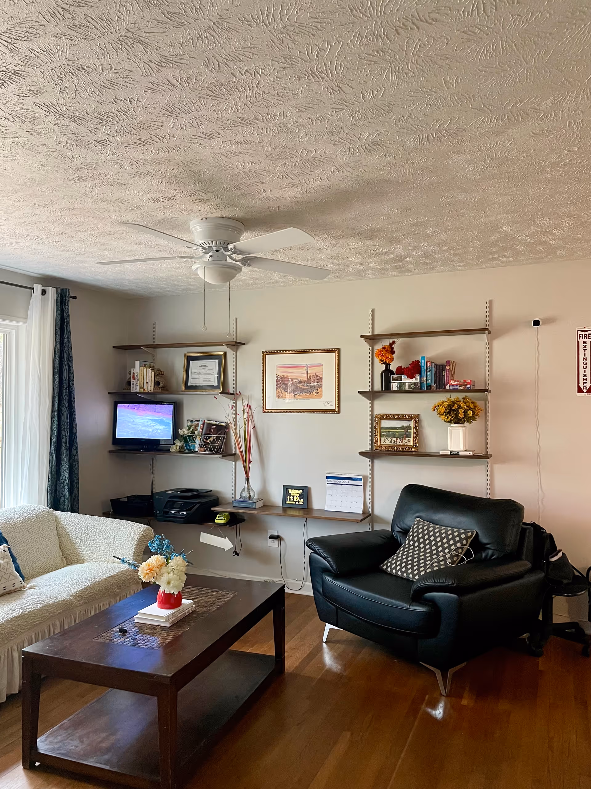 Cozy living room with sofa, leather chair, coffee table, shelves, TV, and ceiling fan.