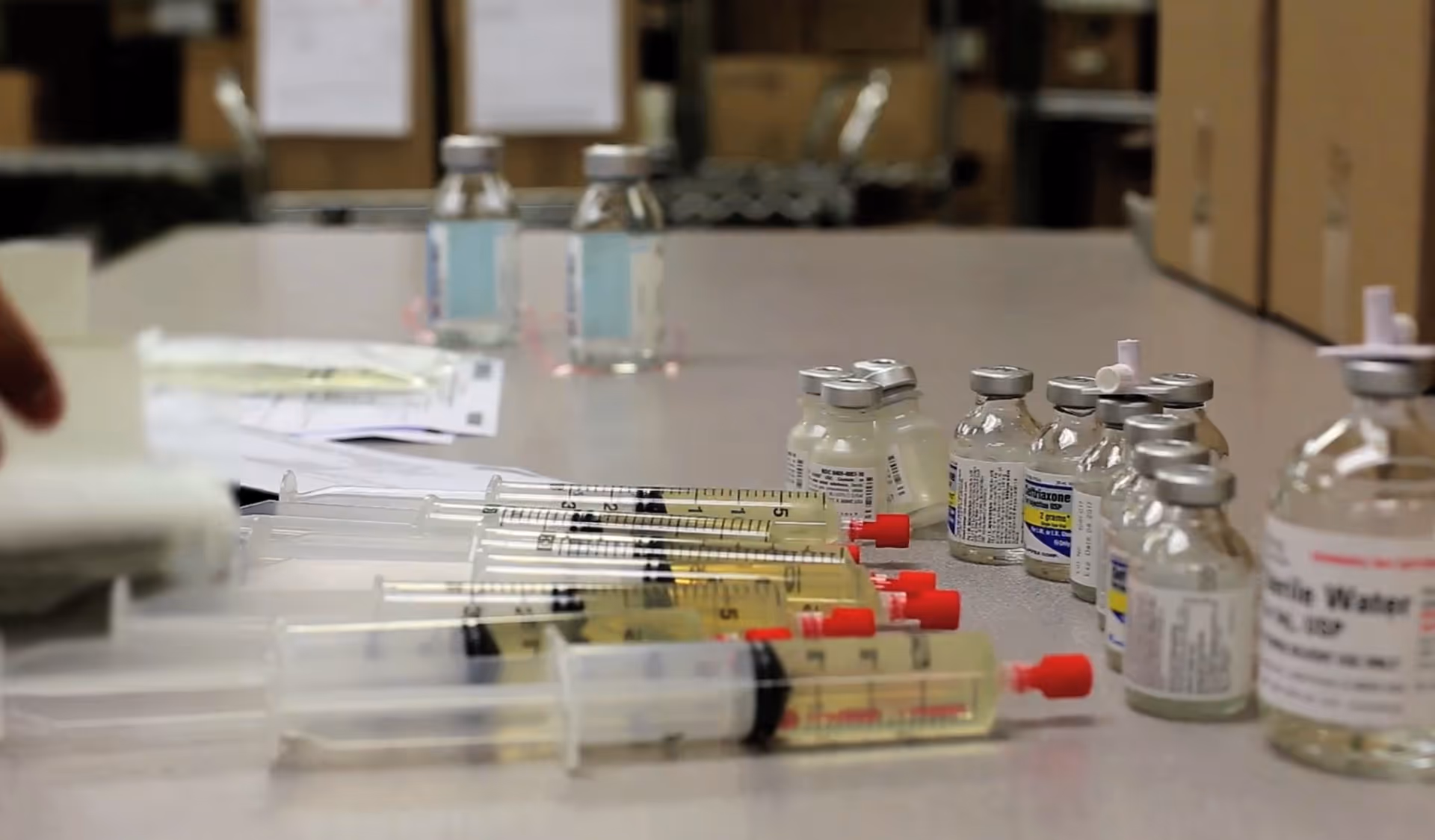 Medical syringes and vaccine vials arranged on a clinical table in a facility.