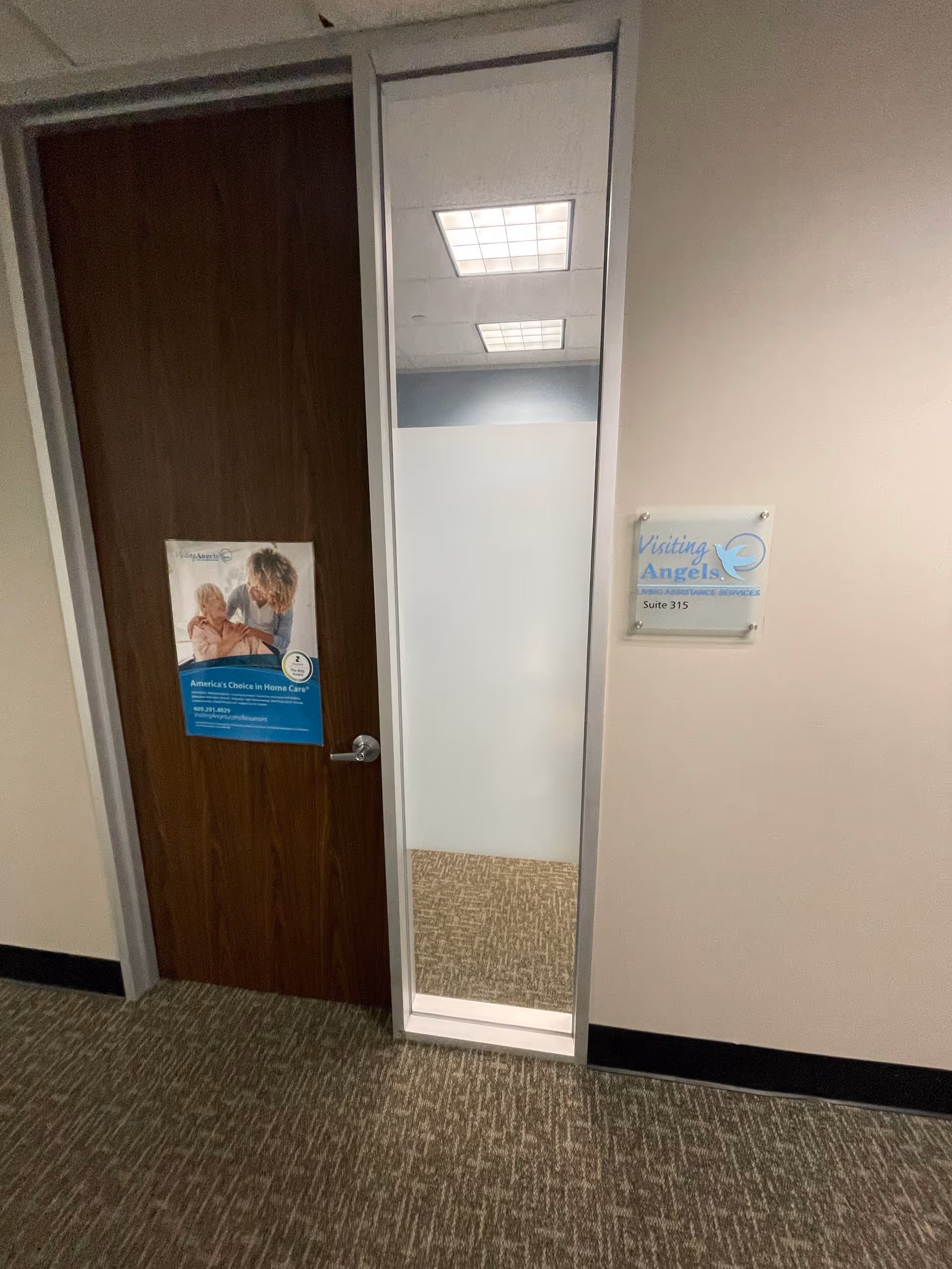 Narrow hallway with a wooden door, a full-length mirror, and a Visiting Angels sign.