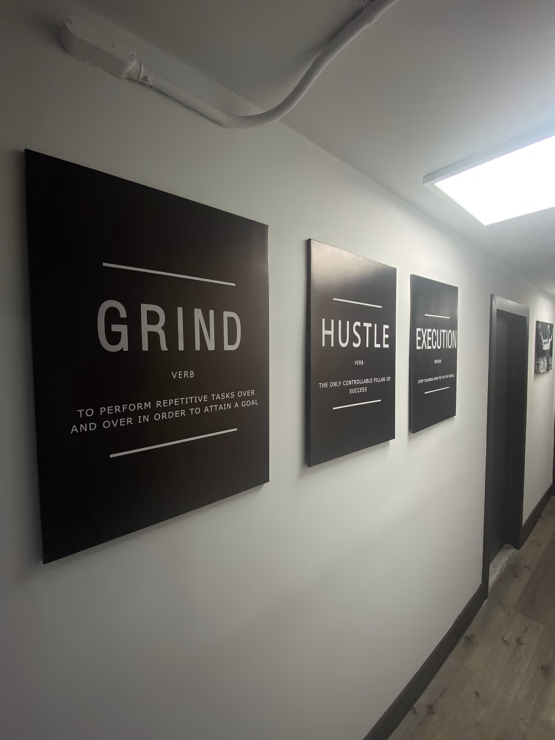 Hallway with black motivational posters labeled GRIND, HUSTLE, and EXECUTION on white walls.