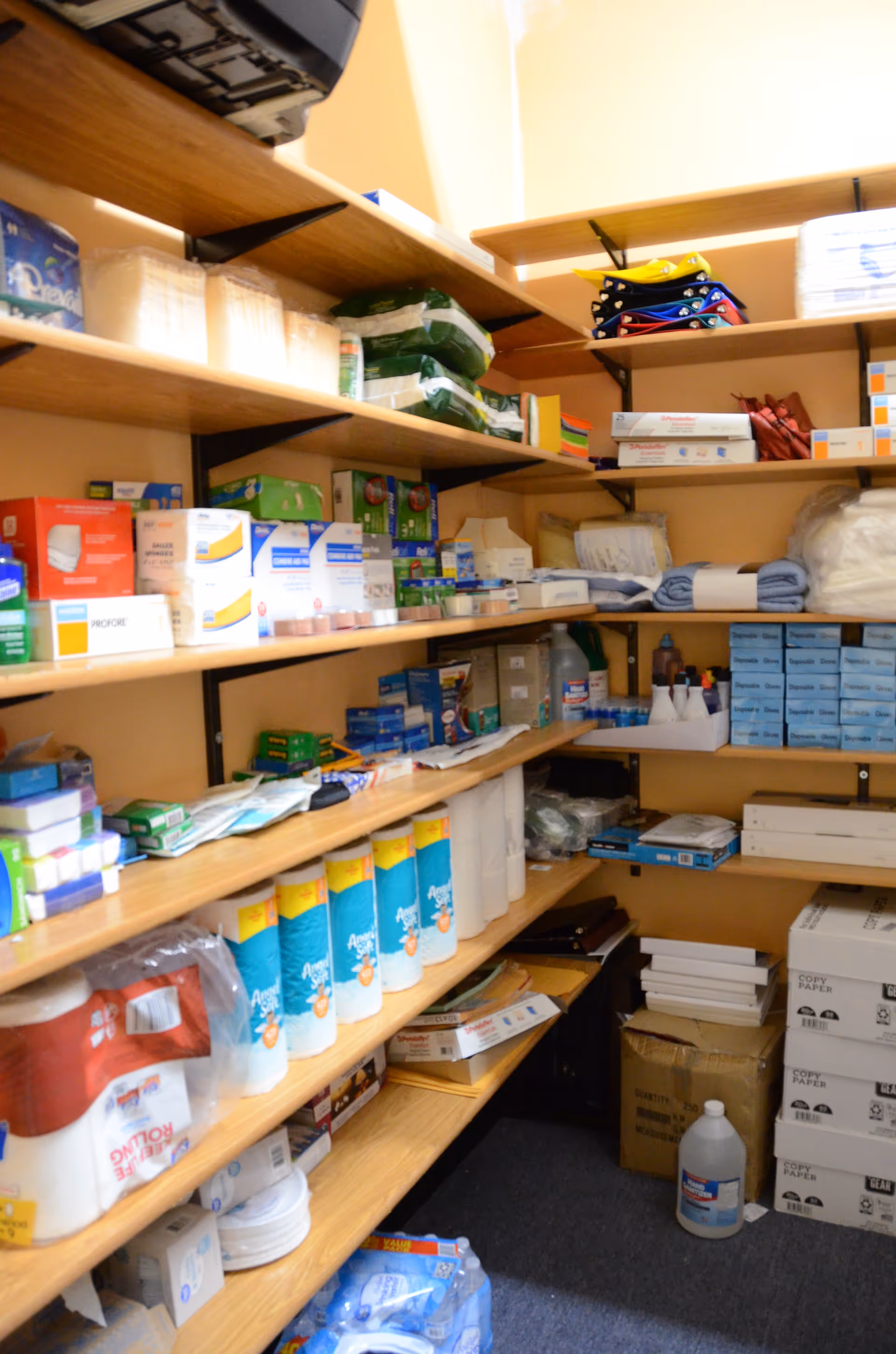 Shelves stocked with medical supplies and paper products in a storage room.