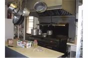 Commercial kitchen area with hanging pots, large stove, hood, and a box-filled counter.