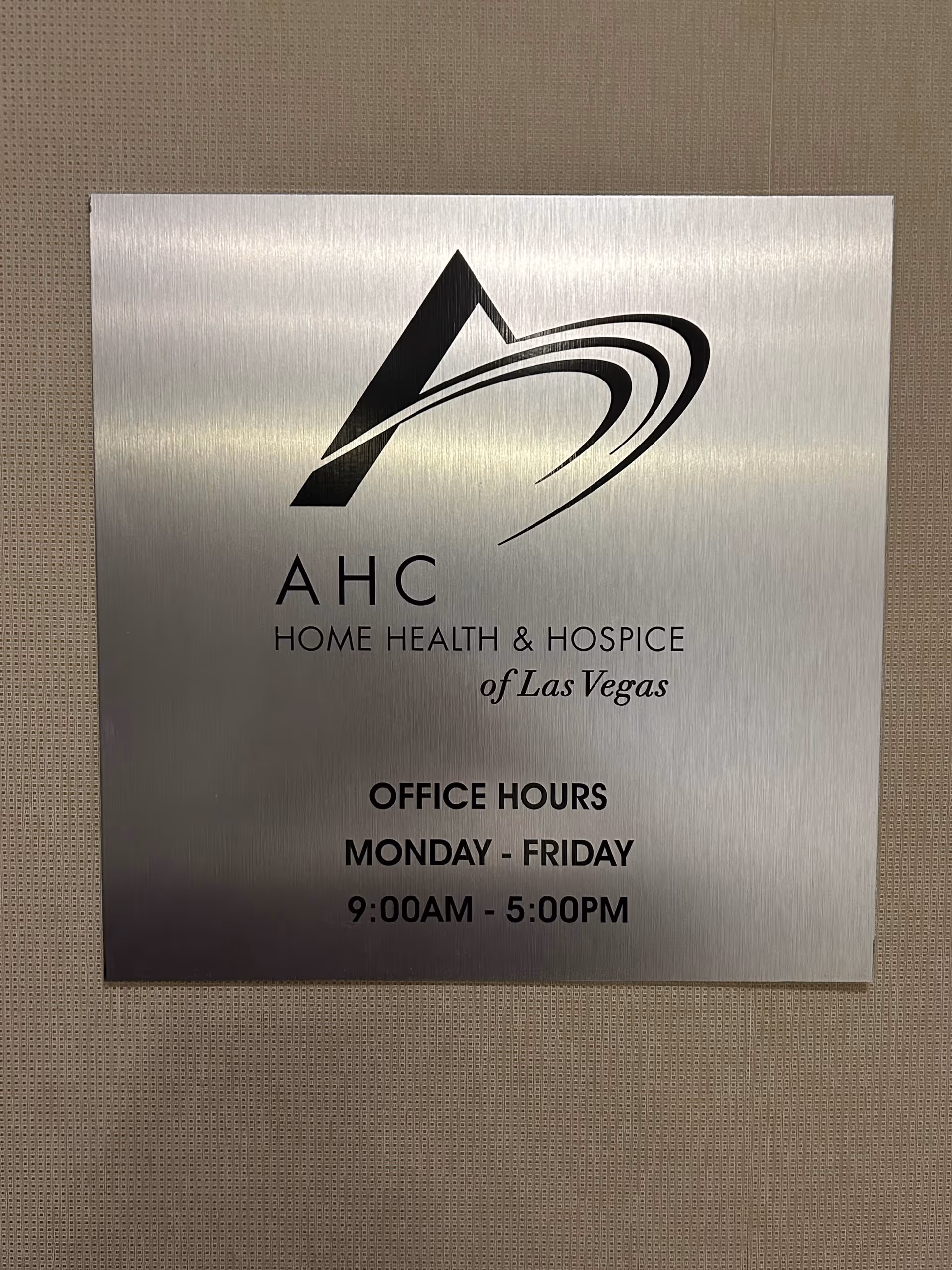 Metal plaque sign displaying AHC Home Health & Hospice of Las Vegas office hours.